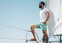 junger bärtiger Mann in Shorts, der auf einer Yacht steht