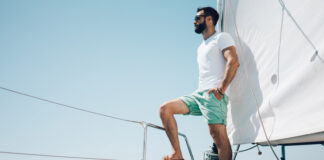 junger bärtiger Mann in Shorts, der auf einer Yacht steht